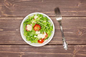 Finished step. ready. recipe step by step arugula salad in a grey ceramic bowl flatlay on brown wood