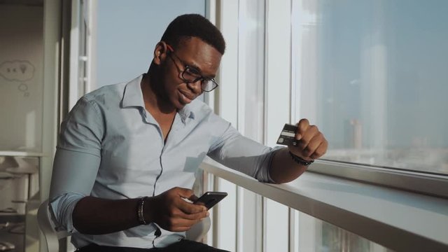man hands holding credit card and entering security code on smart phone for online shopping. African American. Online shopping concept.