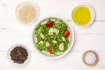 Mixing ingredients step. recipe step by step arugula salad in a grey ceramic bowl flatlay on white wood