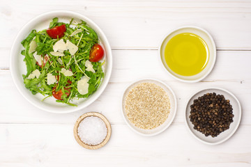 Adding ingredients step. recipe step by step arugula salad in a grey ceramic bowl flatlay on white wood