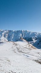 Fototapeta na wymiar Aerial photo of caucasus winter mountainous landscape with mountains ranges. It is winter snowy mountains in Kazbegi, Georgia. There are snow dunes, hills and clear blue sky. Georgian nature.