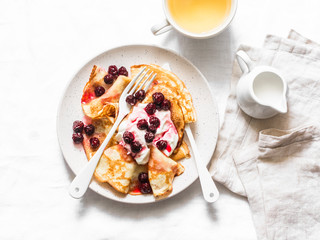Crepes with cherry sauce and cream on a light background, top view. Delicious breakfast, dessert