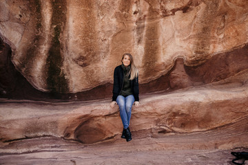 Young Cute Modern Caucasian Woman Smiling in Front of Massive Natural Red Rock Stone Wall Outside in Nature at the State Park