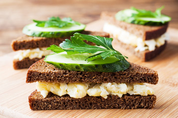 Sandwich with scrambled eggs, cucumbers and parsley on wooden rustic background.