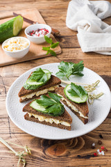 Sandwich with scrambled eggs, cucumbers and parsley on wooden rustic background.