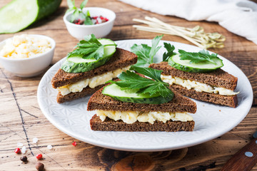 Sandwich with scrambled eggs, cucumbers and parsley on wooden rustic background.