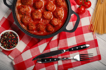 Meatballs in tomato sauce with spices in a frying pan on a white wooden board