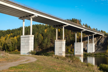 Fototapeta na wymiar large high bridge on concrete columns across the river, on both sides of the river mountains