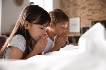 Cute children praying near bed at home