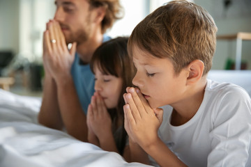 Family praying near bed at home - obrazy, fototapety, plakaty