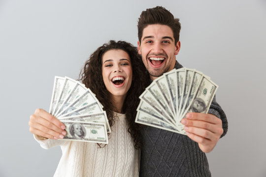 Image of rich man and woman holding fan of dollar money, isolated over gray background
