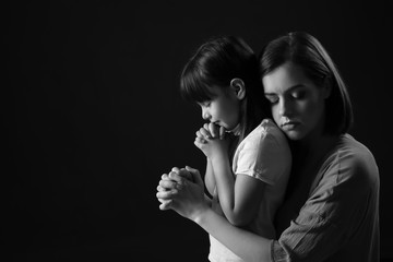Praying mother and daughter on dark background
