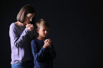 Praying mother and son on dark background