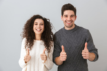 Photo of happy couple man and woman laughing and showing thumbs up at camera, isolated over gray...