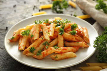 Plate with tasty penne pasta on grey table
