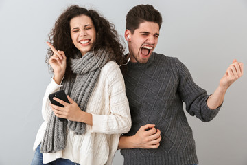 Portrait of playful couple man and woman listening to music with earphones and dancing, isolated over gray background