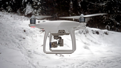 Close up photo of a hovering drone. The Aerial UAV is pictured in a winter, snowy environment in front of some snow covered alpine trees.