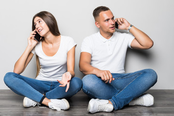 Young couple talking on the phones while sitting on the floor isolated on gray background