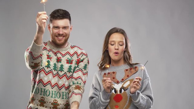 celebration, fun and holidays concept - happy couple wearing knitted sweaters with sparklers dancing at christmas party