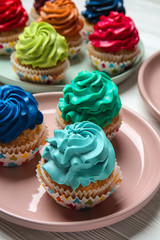 Plates with colorful cupcakes on white wooden table