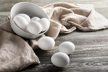 Bowl with raw chicken eggs on wooden table