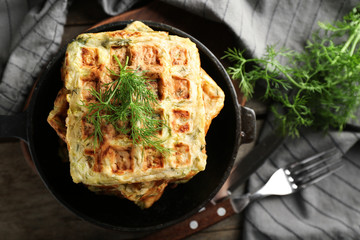 Frying pan with tasty squash waffles on wooden board