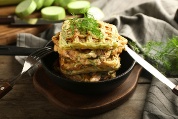 Frying pan with tasty squash waffles on wooden board