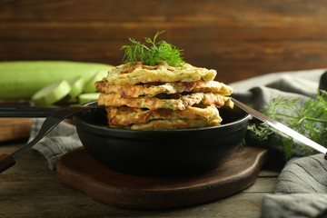 Frying pan with tasty squash waffles on wooden board