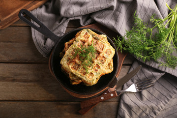 Frying pan with tasty squash waffles on wooden table