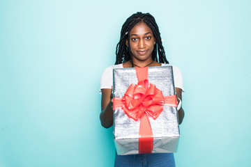 Fototapeta premium Portrait of joyous african woman with afro hairdo holding gift box and smiling in happiness over blue background