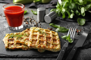 Slate plate with tasty squash waffles and glass of tomato juice on grey table