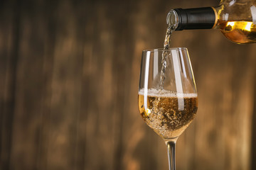 Pouring of white wine from bottle into glass on dark background