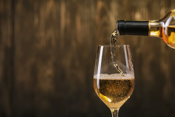 Pouring of white wine from bottle into glass on dark background - obrazy, fototapety, plakaty