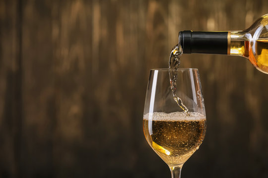 Pouring of white wine from bottle into glass on dark background