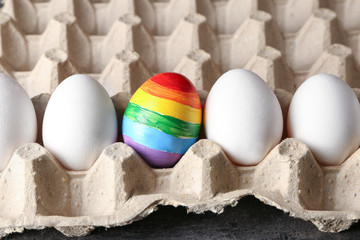 Rainbow painted egg among white ones in carton box. LGBT concept