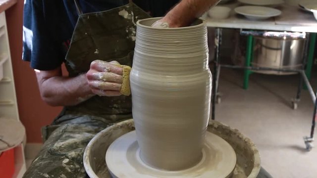 Artist potter in the workshop creating a jug out of earthenware, hands closeup. Twisted potter's wheel. Small aristic craftsmen business concept. 