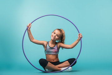 Cheerful little sports girl doing exercises with a hula hoop