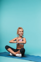 Fototapeta premium Cheerful young sports girl sitting on a fitness mat