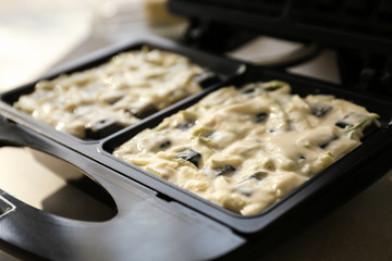 Modern waffle maker with raw dough on table, closeup