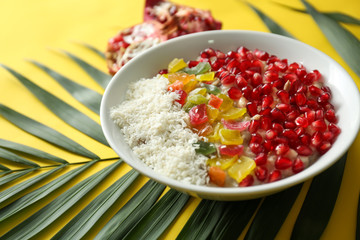 Tasty oatmeal with pomegranate seeds, succades and tropical leaf on color background