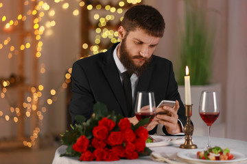 Young man with mobile phone waiting for his girlfriend in restaurant