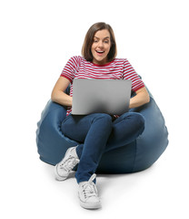 Young woman with laptop sitting on beanbag chair against white background
