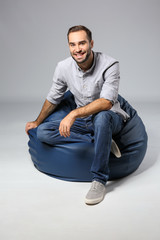 Young man sitting on beanbag chair against grey background