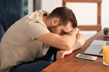 Obraz premium Tired young man sitting at table