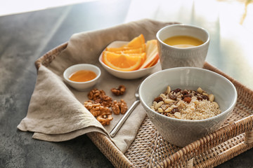 Bowl with tasty oatmeal, cup of tea and fruits on wicker tray