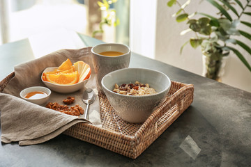 Bowl with tasty oatmeal, cup of tea and fruits on wicker tray