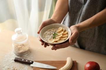 Woman holding bowl with tasty oatmeal and banana slices at table