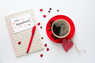 Cup of coffee with notebook and Valentine's Day card on white background