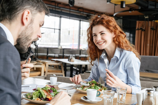 Businesspeople having business lunch at restaurant sitting man eating salad concentrated while woman laughing