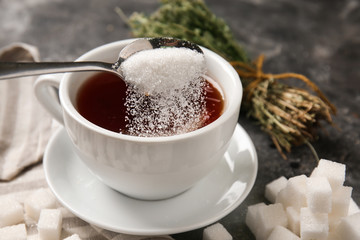 Adding of sugar to cup with aromatic tea on grey table - obrazy, fototapety, plakaty